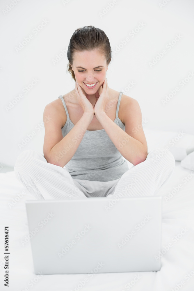 Naklejka premium Smiling casual woman looking at laptop in bed