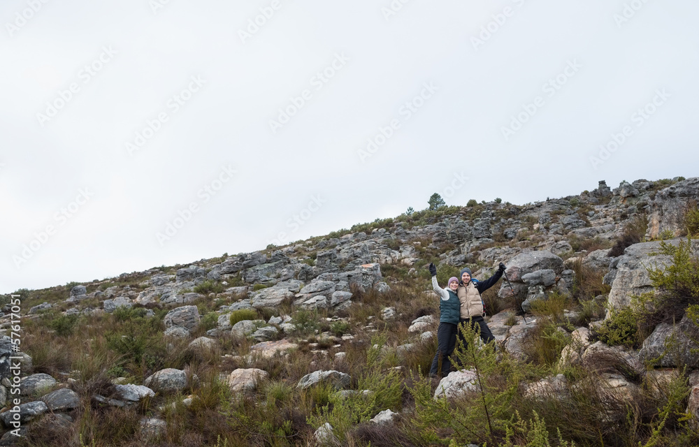 Couple standing on rocky landscape with hands raised against cle