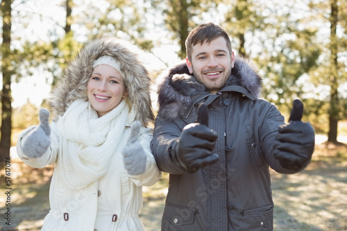 Couple in jackets gesturing thumbs up in the woods