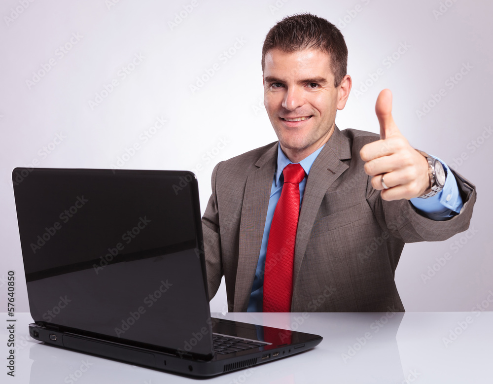 young business man shows thumb up from behind laptop young business man shows thumb up from behind laptop