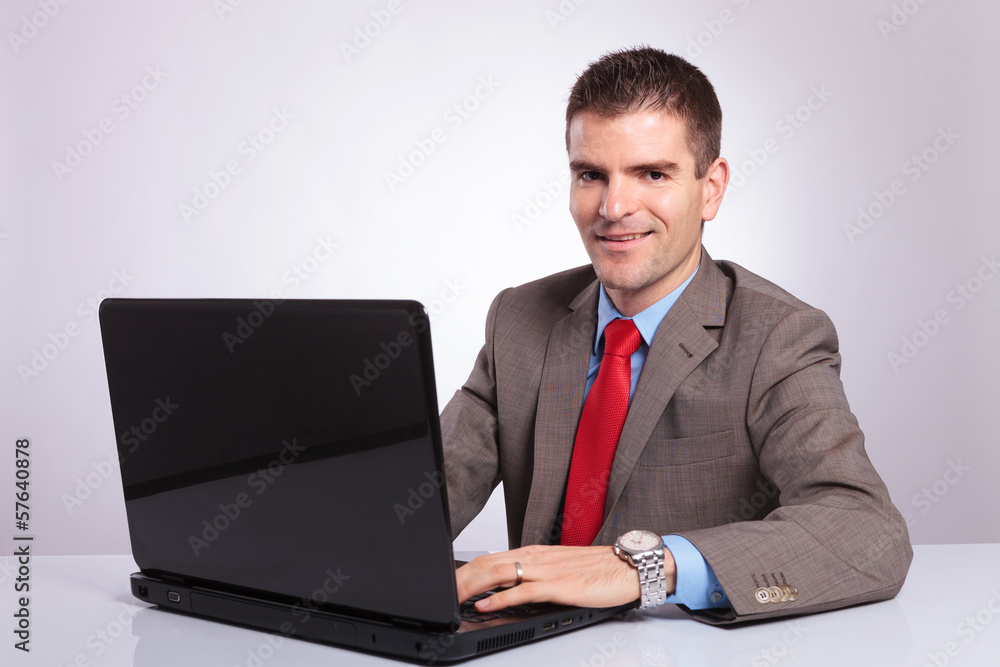 young business man looks at you while working on laptop young business man looks at you while working on laptop