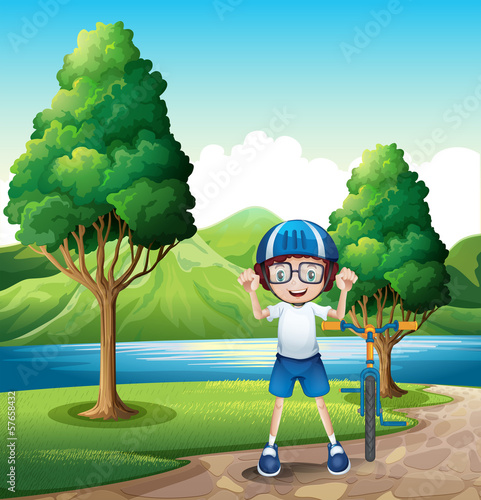 A young boy and his toy bike standing near the trees in the rive