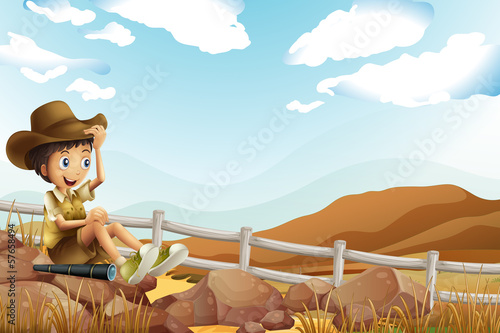 A young explorer sitting above the rock near the wooden fence