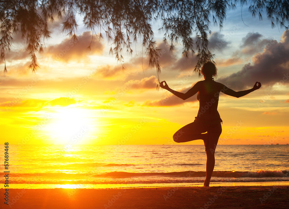Young woman practicing yoga on the beach. Silhouette at sunset.