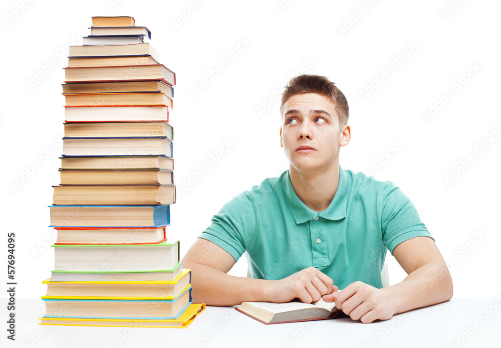 Young frustrated student sitting at the desk with high books sta Young frustrated student sitting at the desk with high books sta