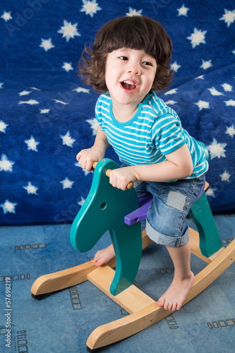 Little boy on toy horse in room with sofa with stars photo