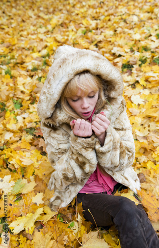 Beautiful girl warms the frozen hands in autumn park