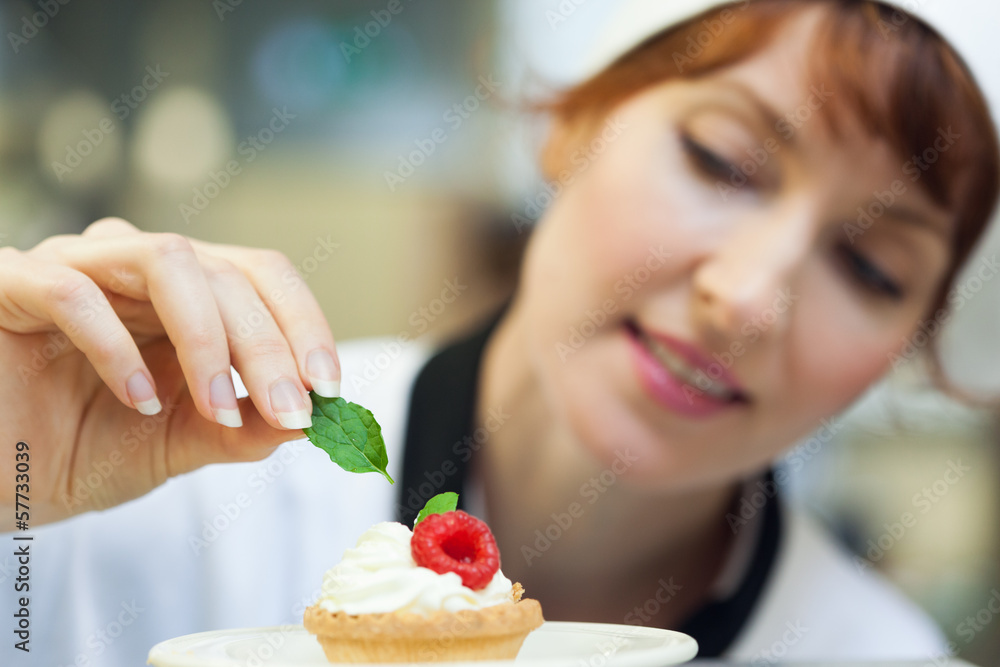 Happy head chef putting mint leaf on little cake Happy head chef putting mint leaf on little cake