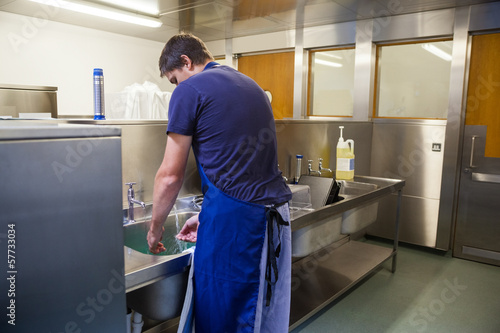 Kitchen porter washing up at sink