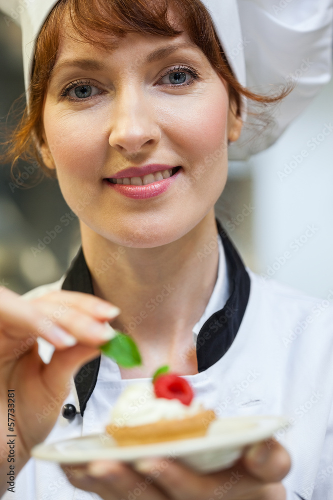 Gorgeous head chef putting mint leaf on little cake on plate Gorgeous head chef putting mint leaf on little cake on plate