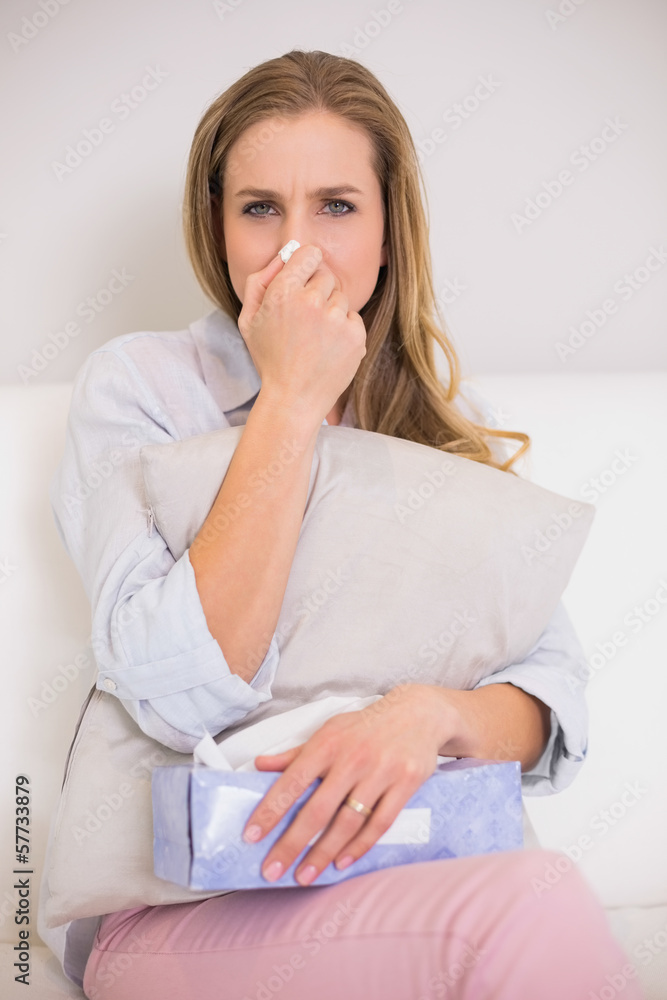 Fototapeta premium Frowning casual blonde sitting on couch blowing nose