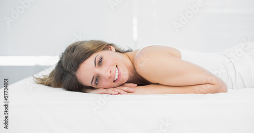 Attractive brunette woman smiling cheerfully at camera lying on