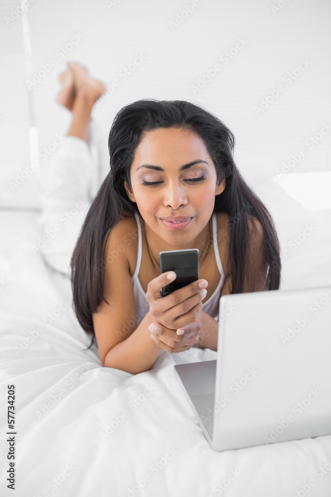 Cute natural woman using her smartphone lying on bed Cute natural woman using her smartphone lying on bed