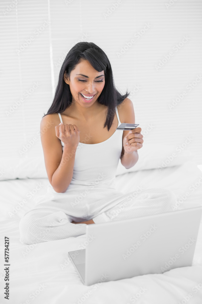 Content cheering woman home shopping with her laptop Content cheering woman home shopping with her laptop