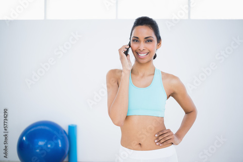 Gleeful sporty woman phoning while standing in fitness hall