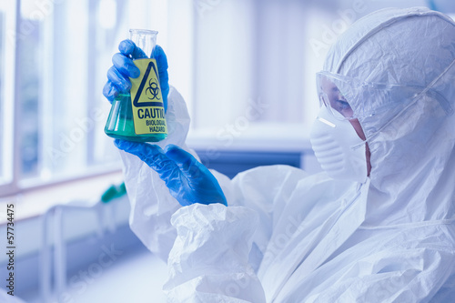 Scientist in protective suit with hazardous chemical in flask at photo