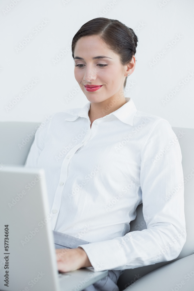 Smiling well dressed woman using laptop on sofa Smiling well dressed woman using laptop on sofa