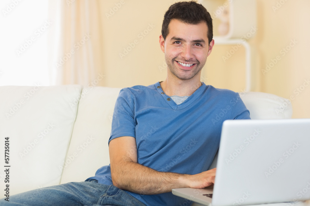 Casual smiling man sitting on couch using laptop Casual smiling man sitting on couch using laptop