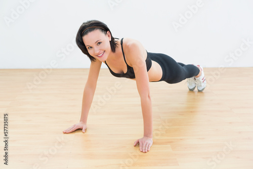 Beautiful sporty woman doing push ups in fitness studio