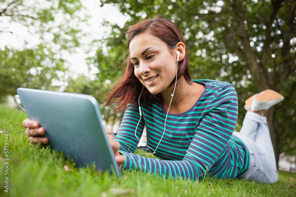 Smiling casual student lying on grass using tablet Smiling casual student lying on grass using tablet