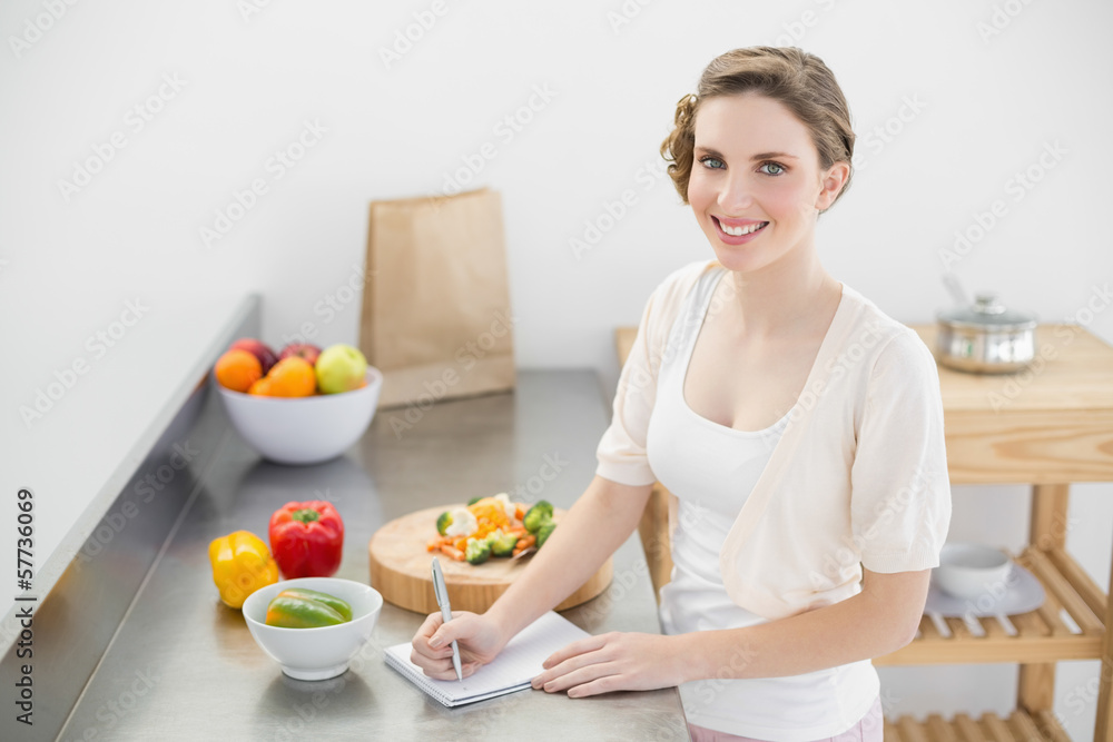 Lovely woman standing in her kitchen writing a shopping list