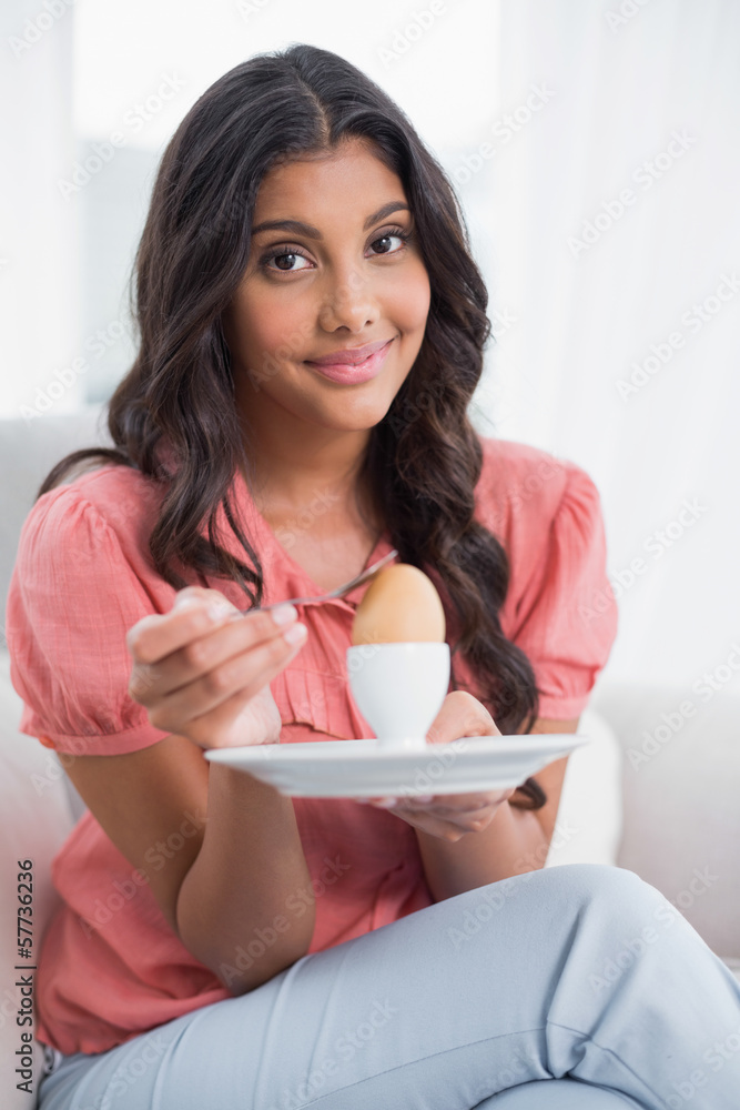 Content cute brunette sitting on couch holding hard boiled egg Content cute brunette sitting on couch holding hard boiled egg