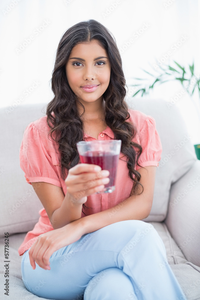 Content cute brunette sitting on couch holding glass of juice