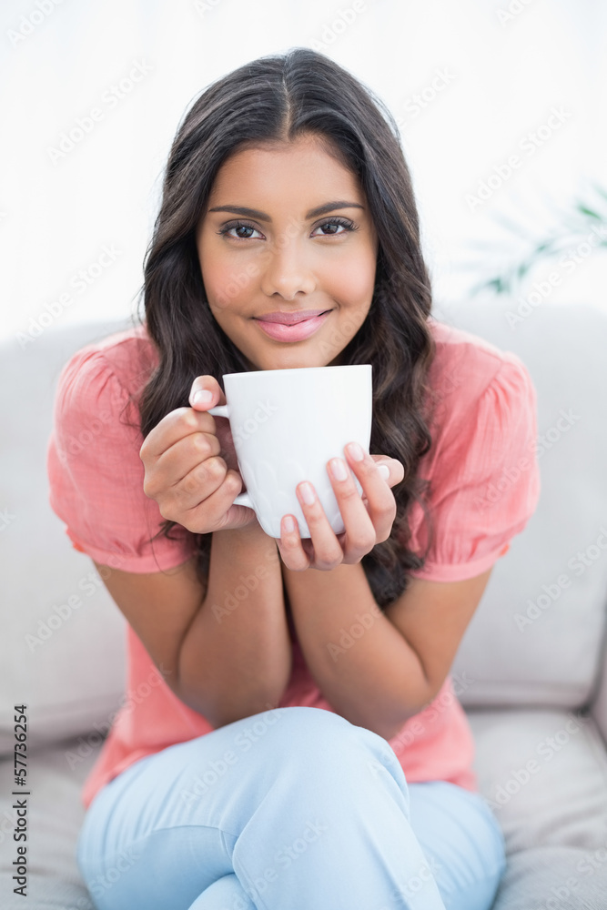 Content cute brunette sitting on couch holding mug Content cute brunette sitting on couch holding mug