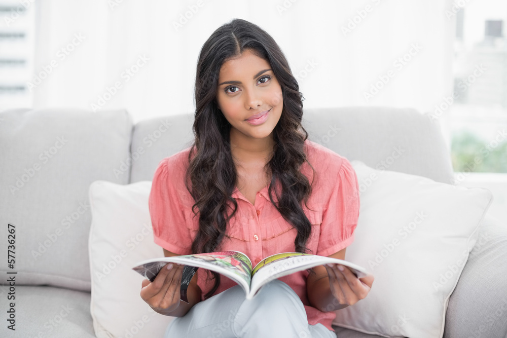 Happy cute brunette sitting on couch holding magazine Happy cute brunette sitting on couch holding magazine