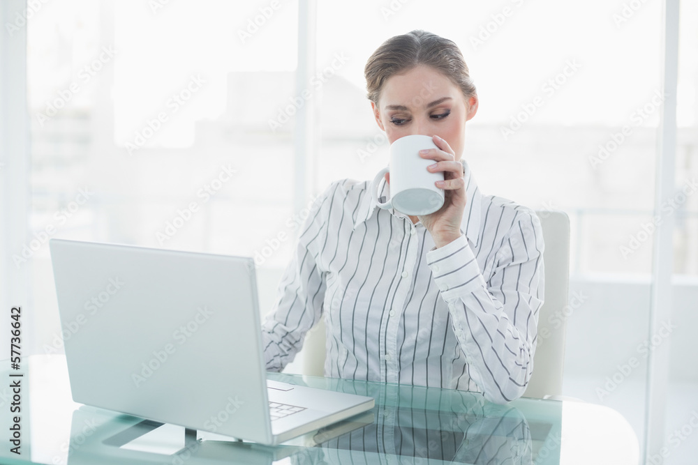 Beautiful businesswoman sitting at her desk drinking from cup Beautiful businesswoman sitting at her desk drinking from cup