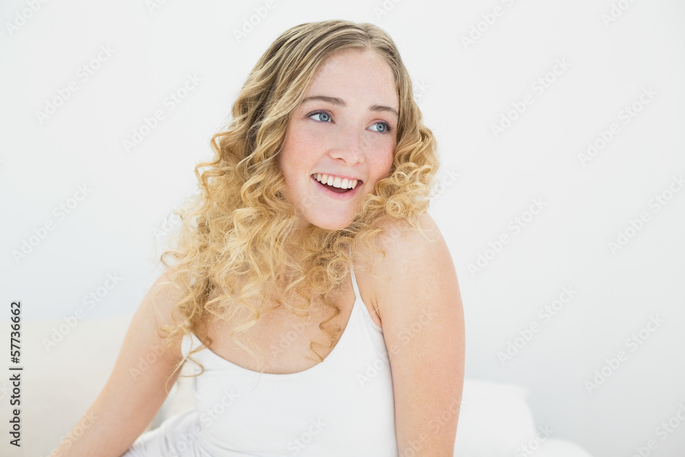 Pretty gleeful blonde sitting on bed looking away Pretty gleeful blonde sitting on bed looking away