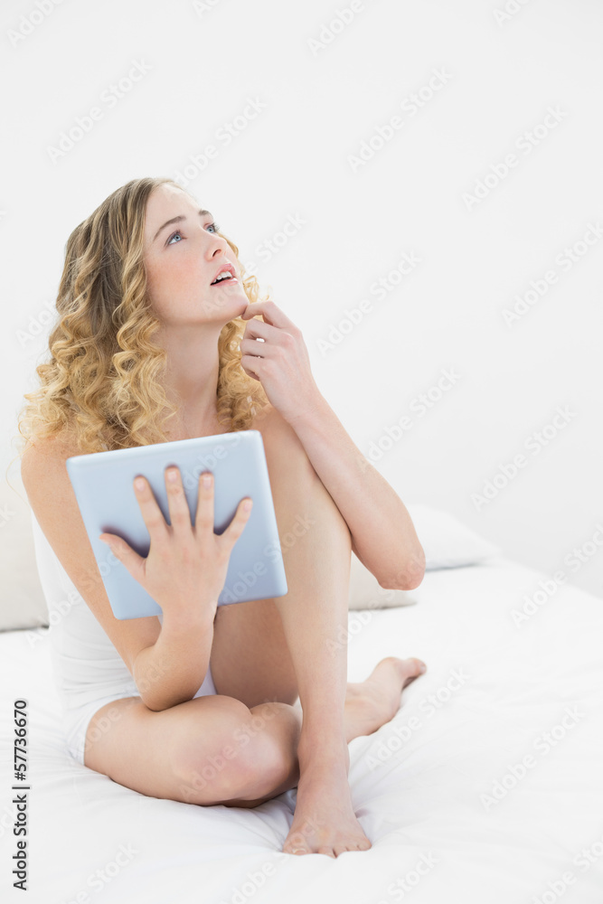 Pretty thoughtful blonde sitting on bed using tablet Pretty thoughtful blonde sitting on bed using tablet