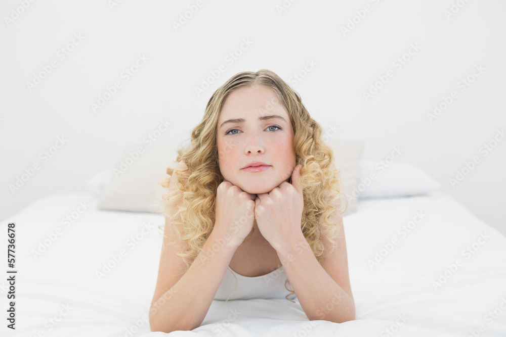 Pretty frowning blonde lying on bed looking at camera