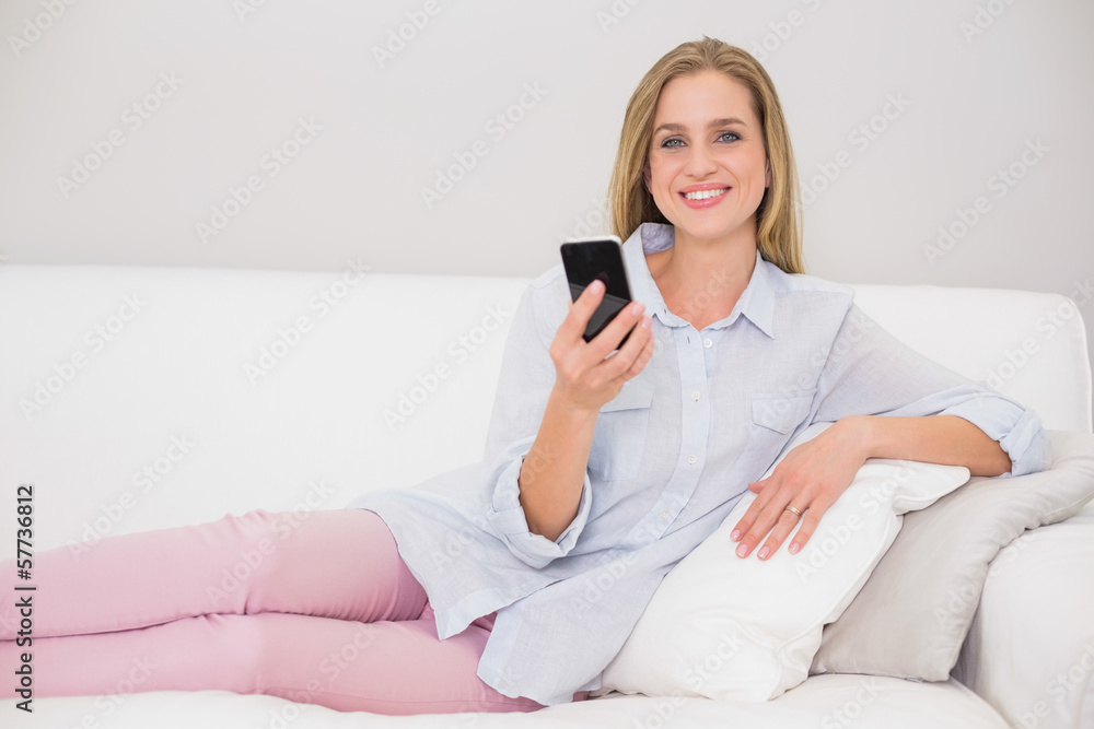Happy casual blonde relaxing on couch holding smartphone Happy casual blonde relaxing on couch holding smartphone