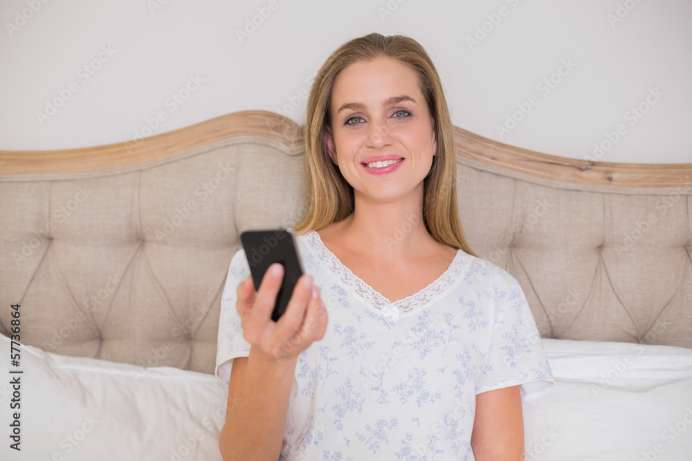 Natural happy woman sitting in bed holding smartphone Natural happy woman sitting in bed holding smartphone
