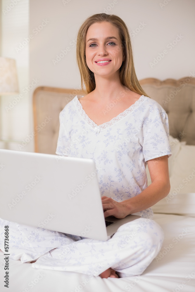 Natural cheerful woman sitting on bed using laptop Natural cheerful woman sitting on bed using laptop