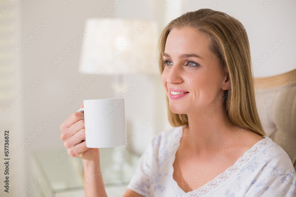 Natural happy woman sitting on bed holding mug Natural happy woman sitting on bed holding mug