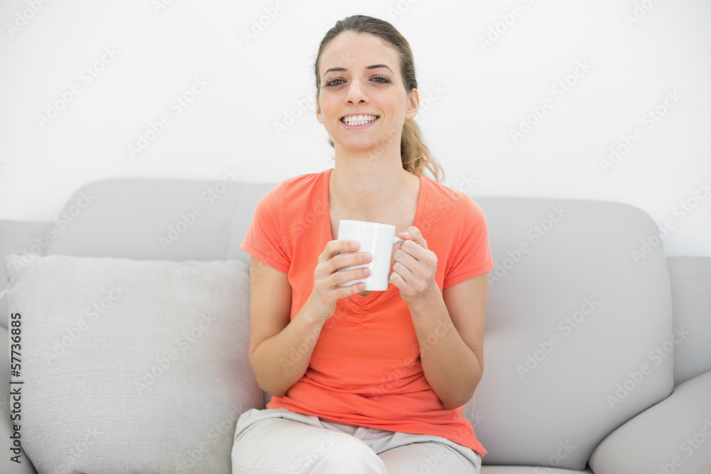 Cheerful beautiful woman holding a cup sitting on couch Cheerful beautiful woman holding a cup sitting on couch