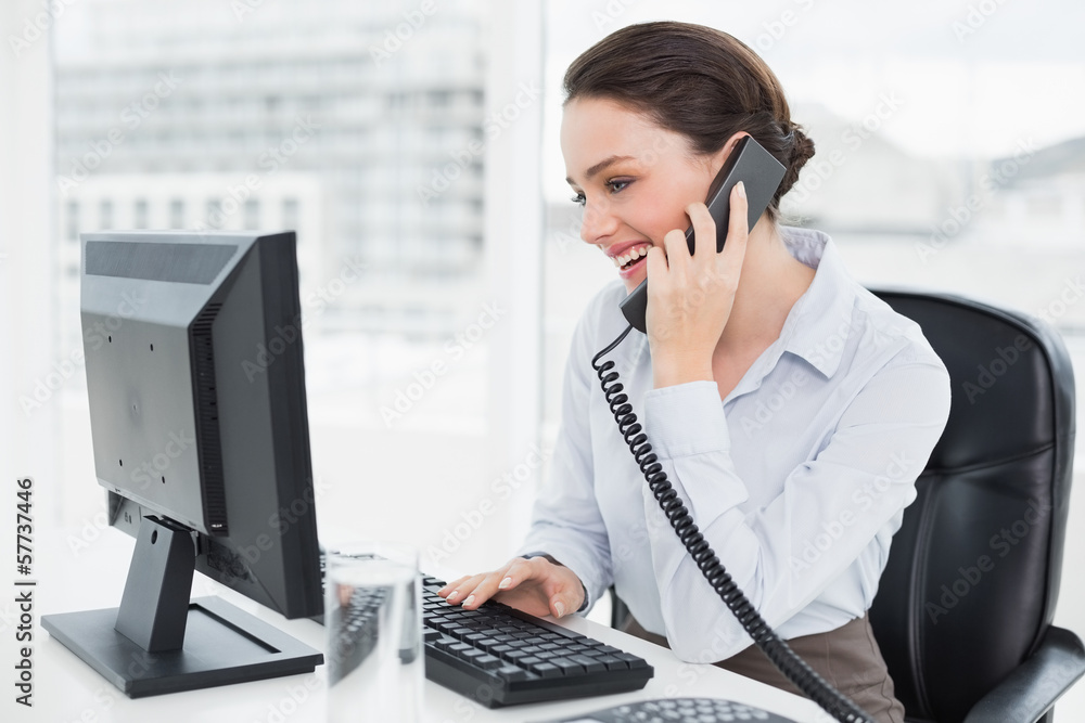 Smiling businesswoman using landline phone and computer in offic Smiling businesswoman using landline phone and computer in offic