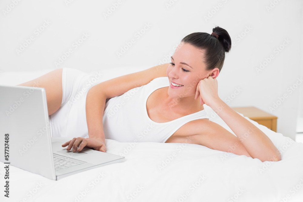 Obraz premium Casual smiling woman using laptop in bed