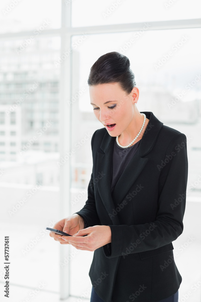 Shocked elegant businesswoman looking at mobile phone