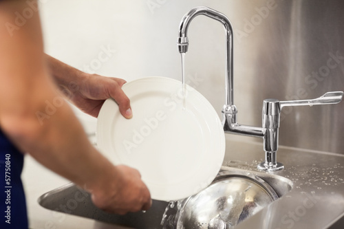 Kitchen porter cleaning white plates in sink