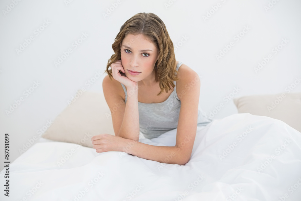 Serious slender woman sitting on her bed under the cover
