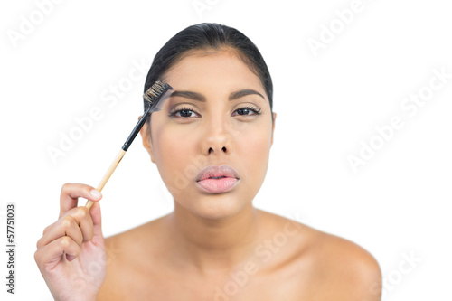 Serious nude brunette using eyebrow brush