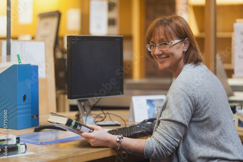 Smiling female librarian holding a book standing behind the desk photo