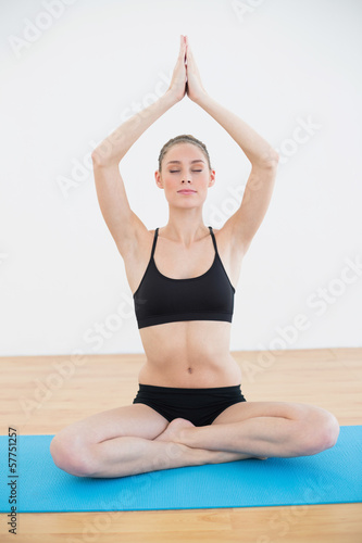 Calm slender woman sitting in lotus position on blue exercise ma