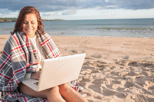 Woman covered with blanket using laptop at beach