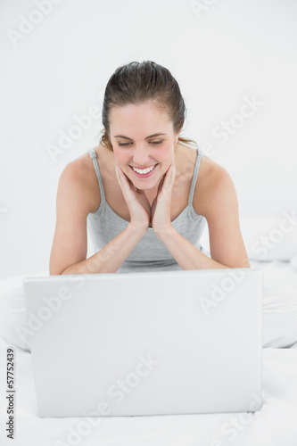 Smiling casual woman looking at laptop in bed