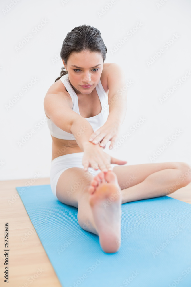Fototapeta premium Toned young woman doing the hamstring stretch on exercise mat in