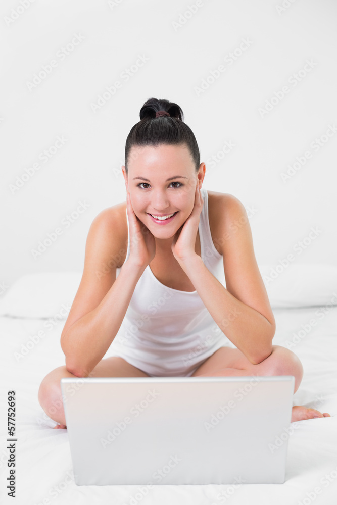 Casual smiling woman with laptop sitting on bed Casual smiling woman with laptop sitting on bed